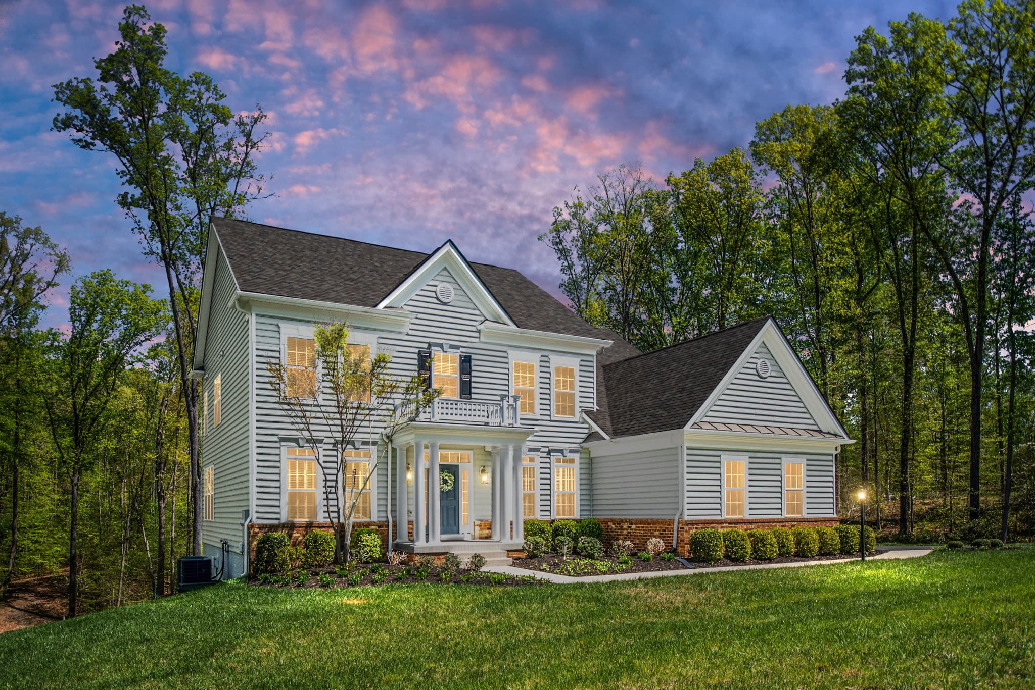 A warm colonial home at twilight with a pink sky and softly glowing golden windows in the Mid-Atlantic
